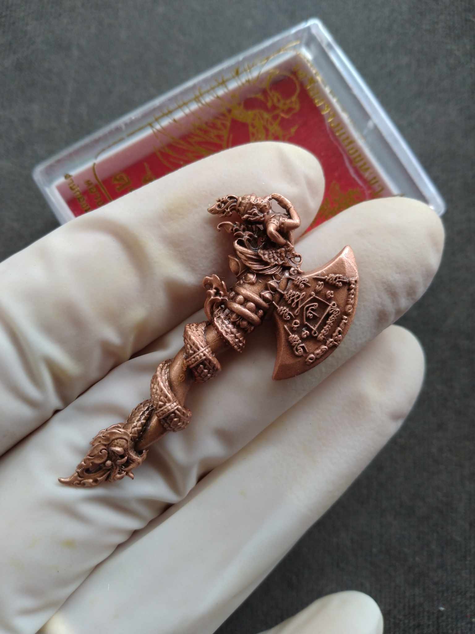 Copper carved pendant held in gloved hand featuring serpent and deity motifs blessed Thai Sky Axe for luck
