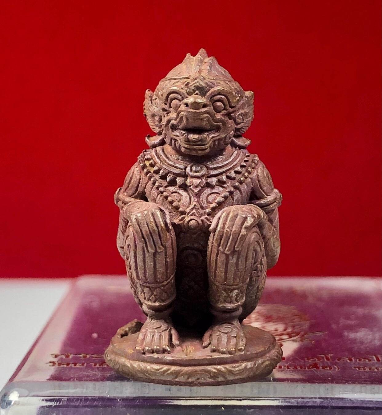 Small brown Hanuman Maha Prap Amulet figurine with intricate carvings on red background