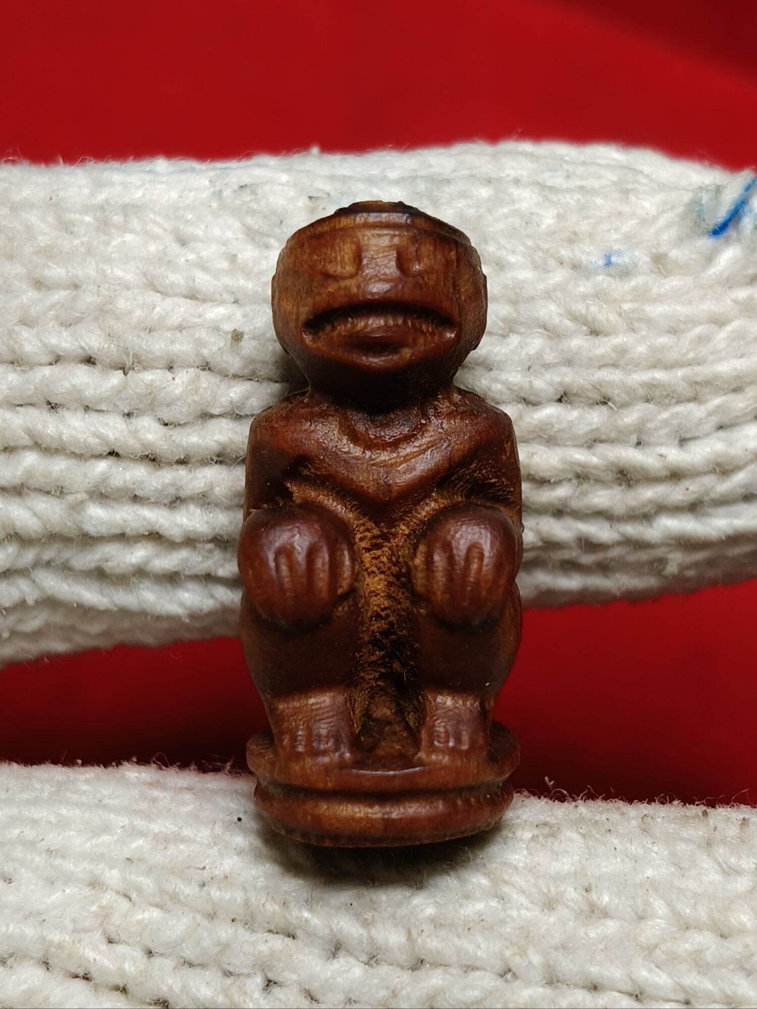 Hand carved wooden Hanuman monkey god amulet pendant of seated monkey figure held by gloved fingers