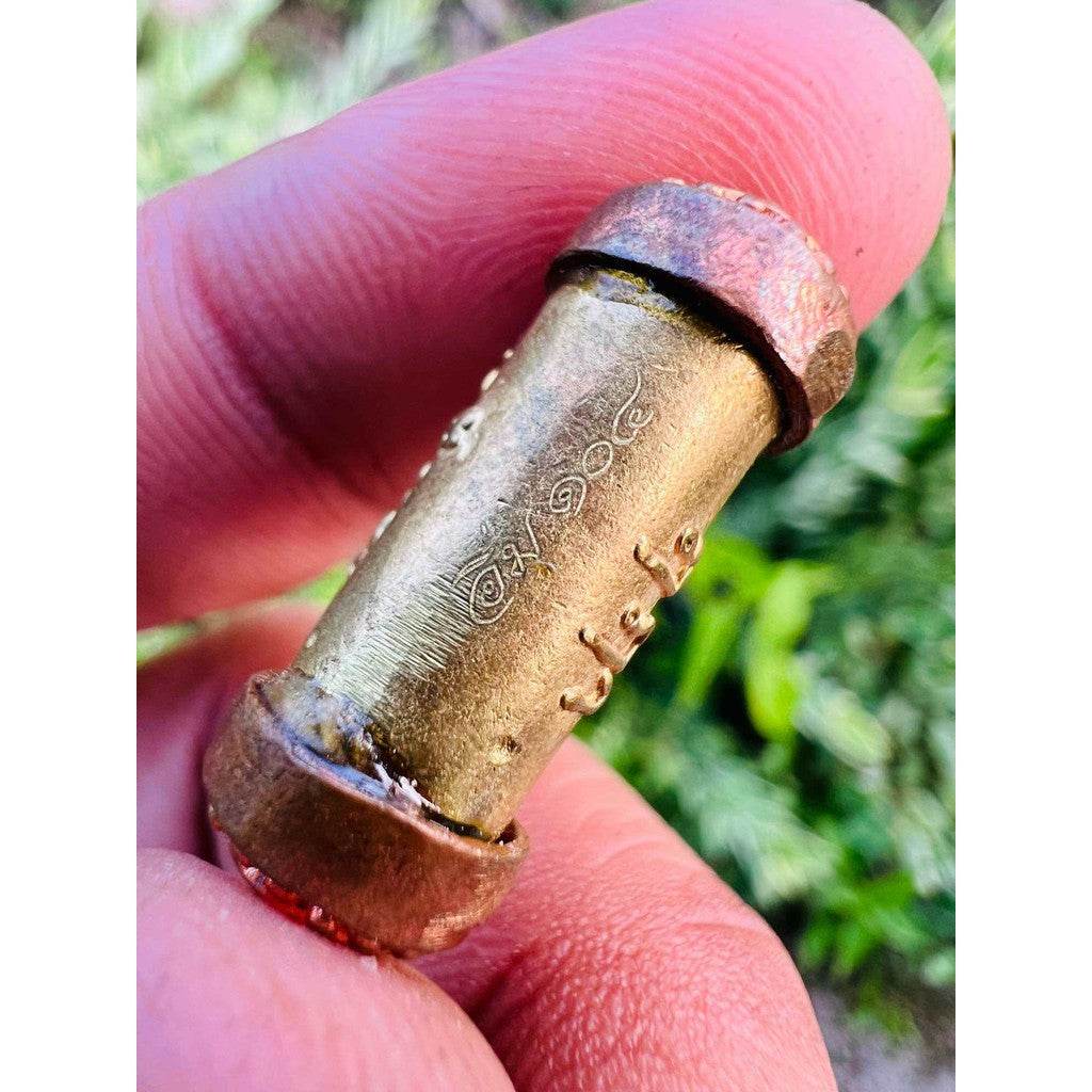 Mangkhang Ramruai amulet for prosperity small engraved brass cylinder with copper caps held between fingers