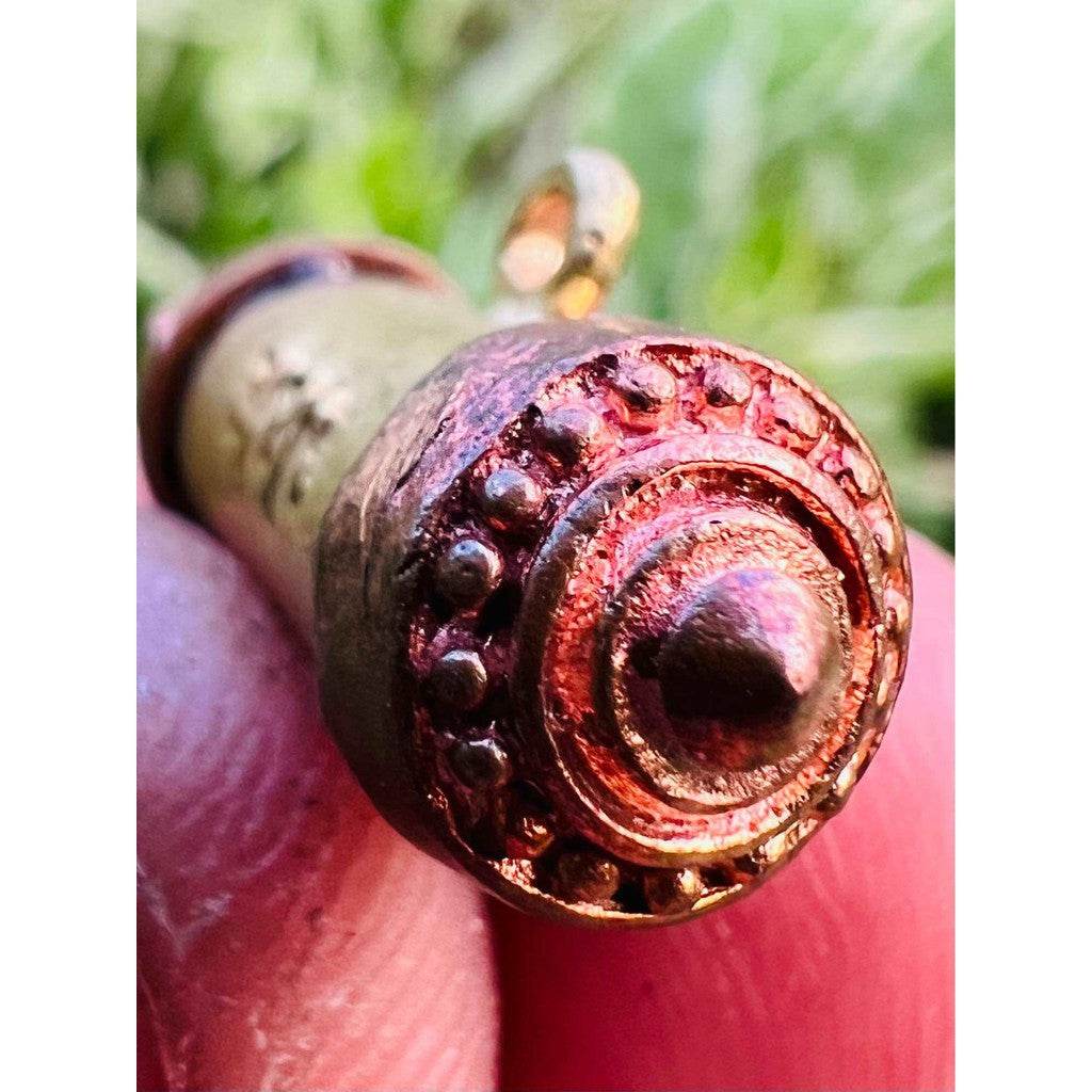 Close up of Mangkhang Ramruai amulet for prosperity brass pendant with ornate beaded domed end held between fingers