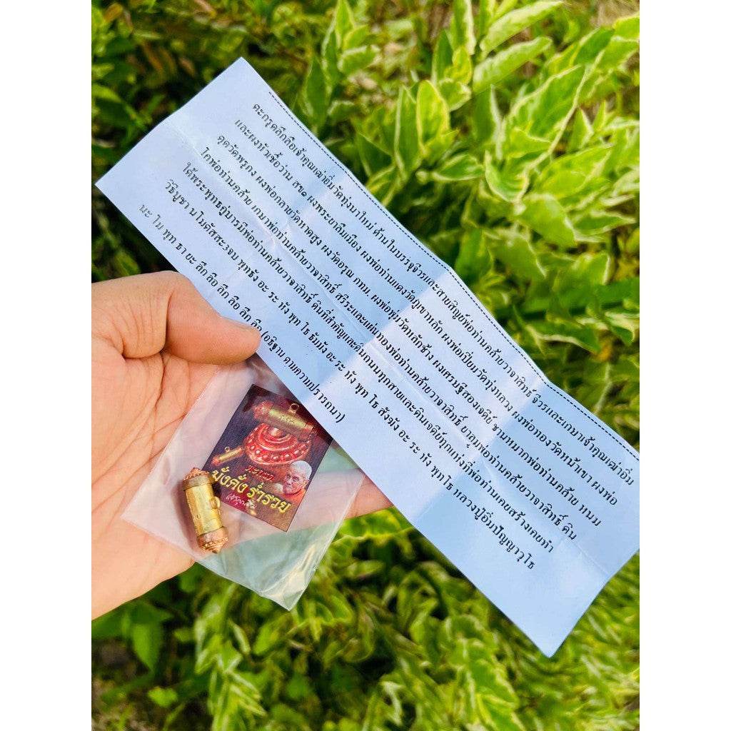 Hand holding Mangkhang Ramruai amulet for prosperity in plastic pouch with blessing card and prayer sheet
