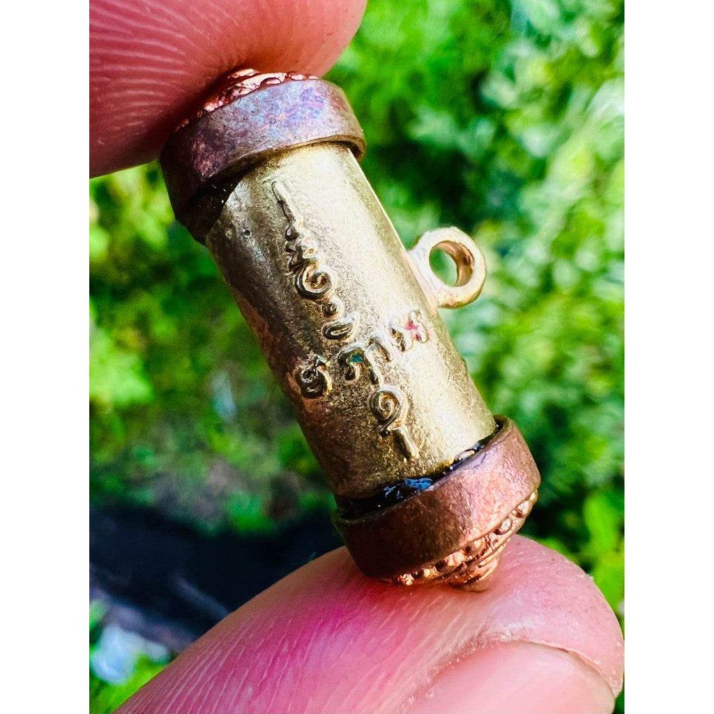 Close up of Mangkhang Ramruai amulet for prosperity brass cylinder with engraved Thai script and copper end caps