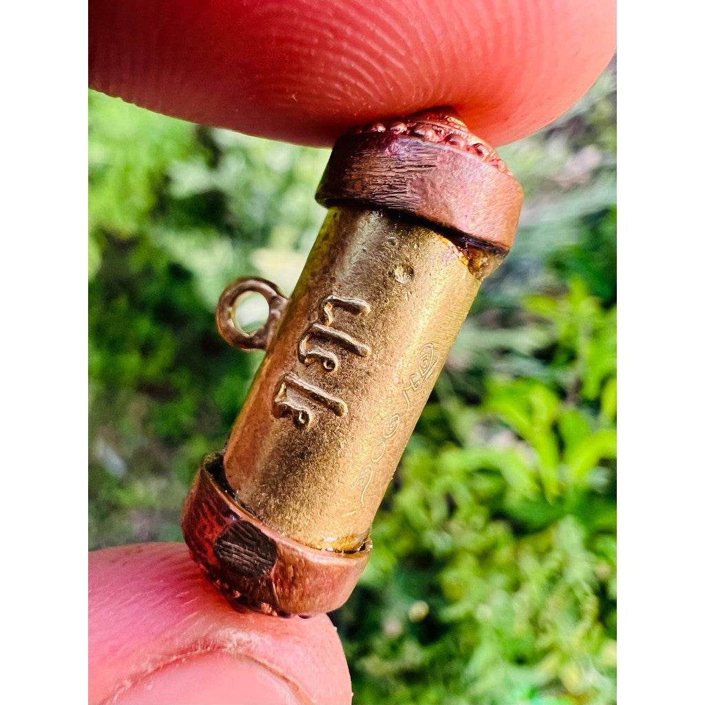 Mangkhang Ramruai amulet for prosperity brass and copper cylinder talisman with Thai script held between fingers