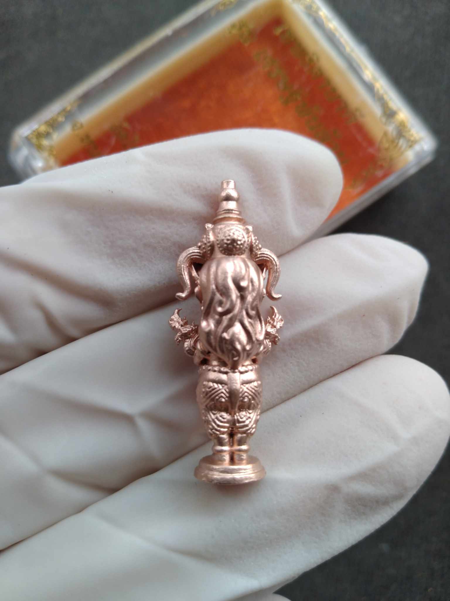 Gloved hand holding a copper Nakee Goddess – Billionaire Edition Sacred Thai Amulet for Wealth miniature statue