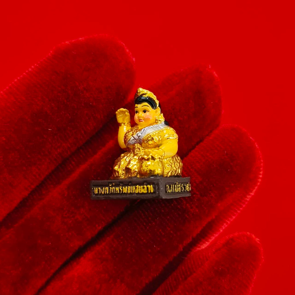 Nang Kwak amulet for wealth small gold figurine held on red velvet glove showing Thai script base