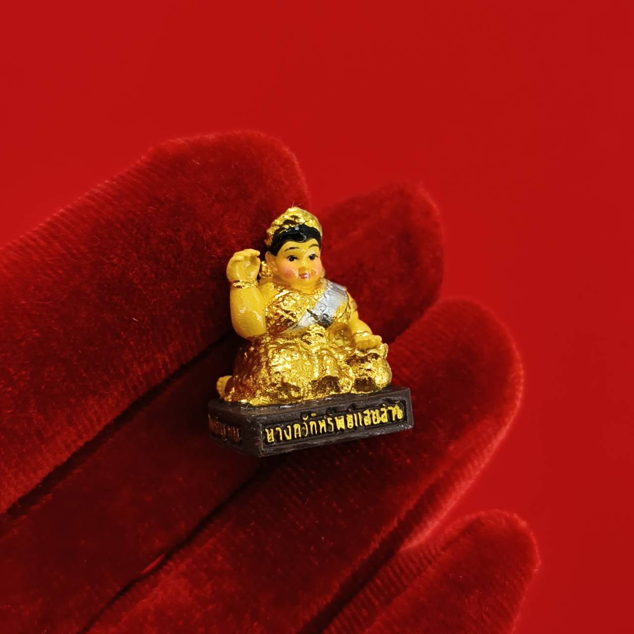 Thai Blessing Co Nang Kwak amulet for wealth miniature gold statue on black base held on red velvet glove