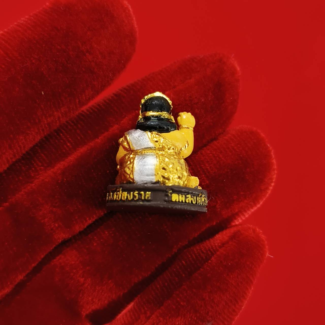 Thai Nang Kwak amulet for wealth small gold seated figurine on red velvet glove background