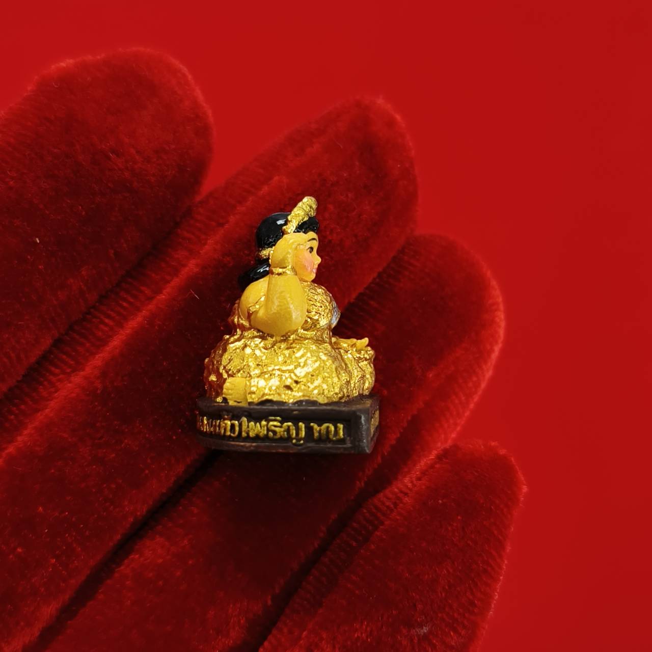 Nang Kwak amulet for wealth gold figurine on pedestal with Thai script held on red velvet glove