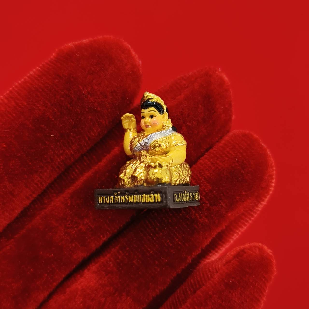 Thai Blessing Co small gold Nang Kwak amulet for wealth figurine held on red velvet glove against red background