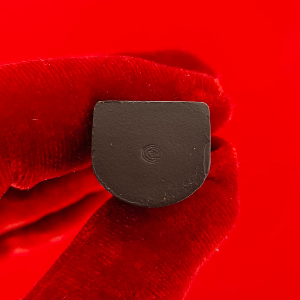 Close up of small black Nang Kwak amulet for wealth held by red gloved fingers on red background