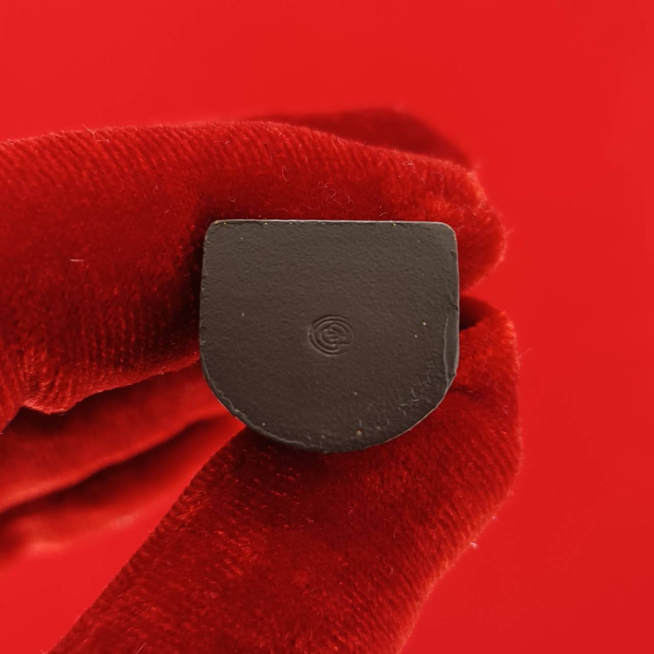 Close up of small black Nang Kwak amulet for wealth held by red gloved fingers on red background