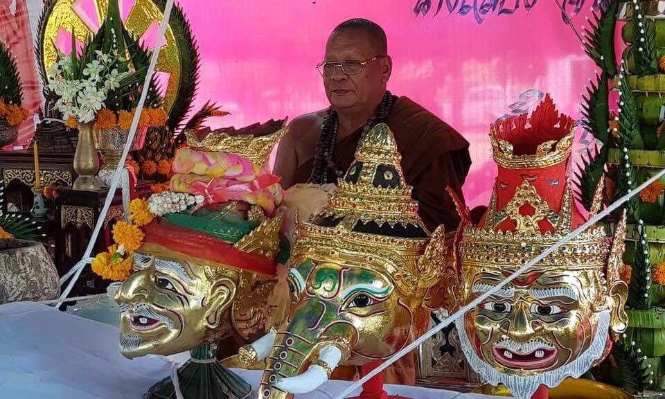 Narai on Garuda amulet displayed with gold ceremonial Thai masks and a Buddhist monk at shrine