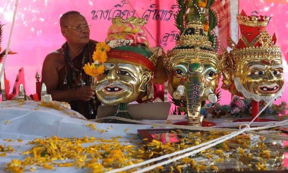 Thai ornate gold amulets displayed on altar with marigold petals and monk in background Narai on Garuda amulet