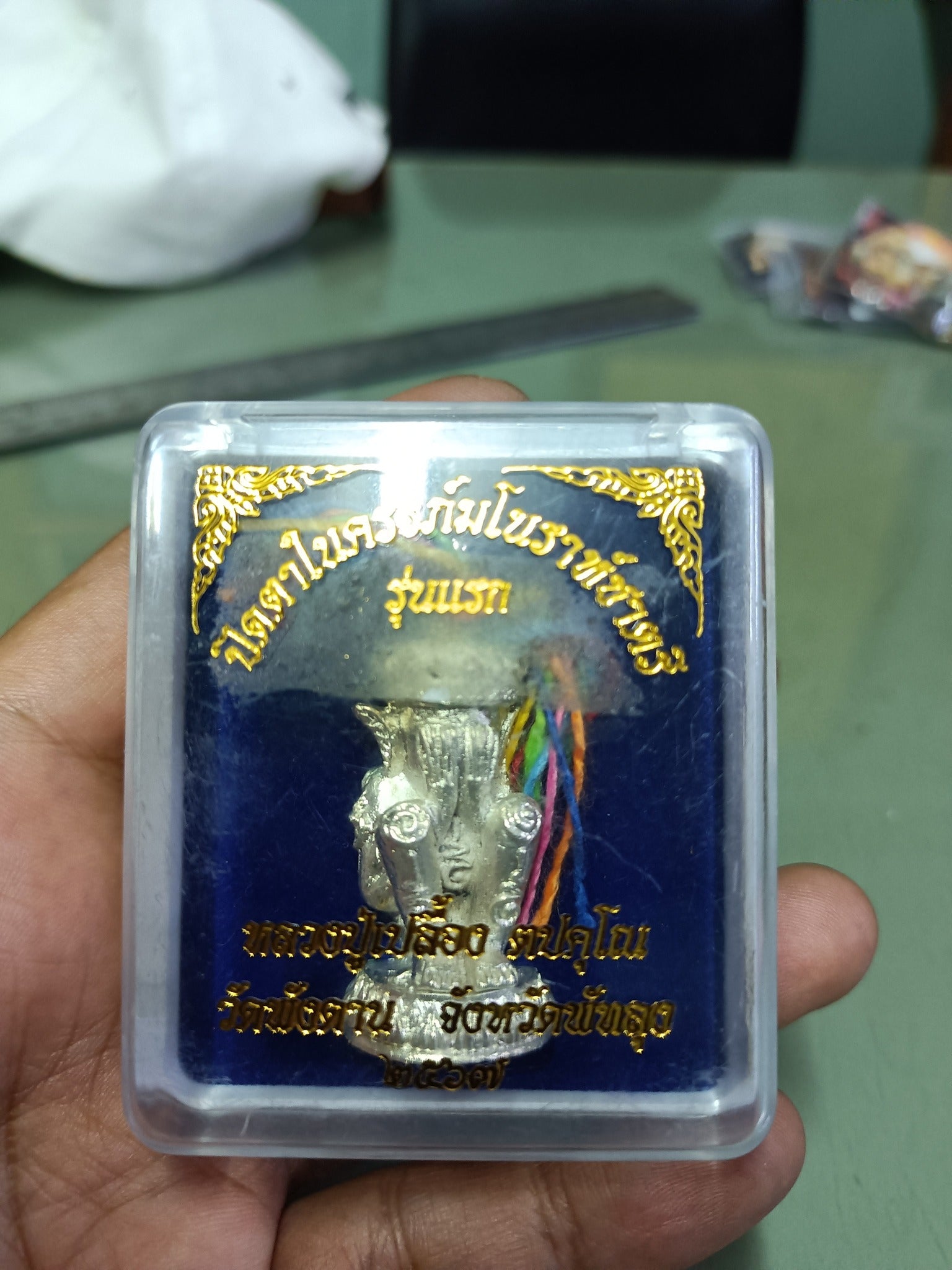 Norah Chatri Pi Takta amulet for protection. Silver Thai statue in clear plastic case with gold script and multicolor threads