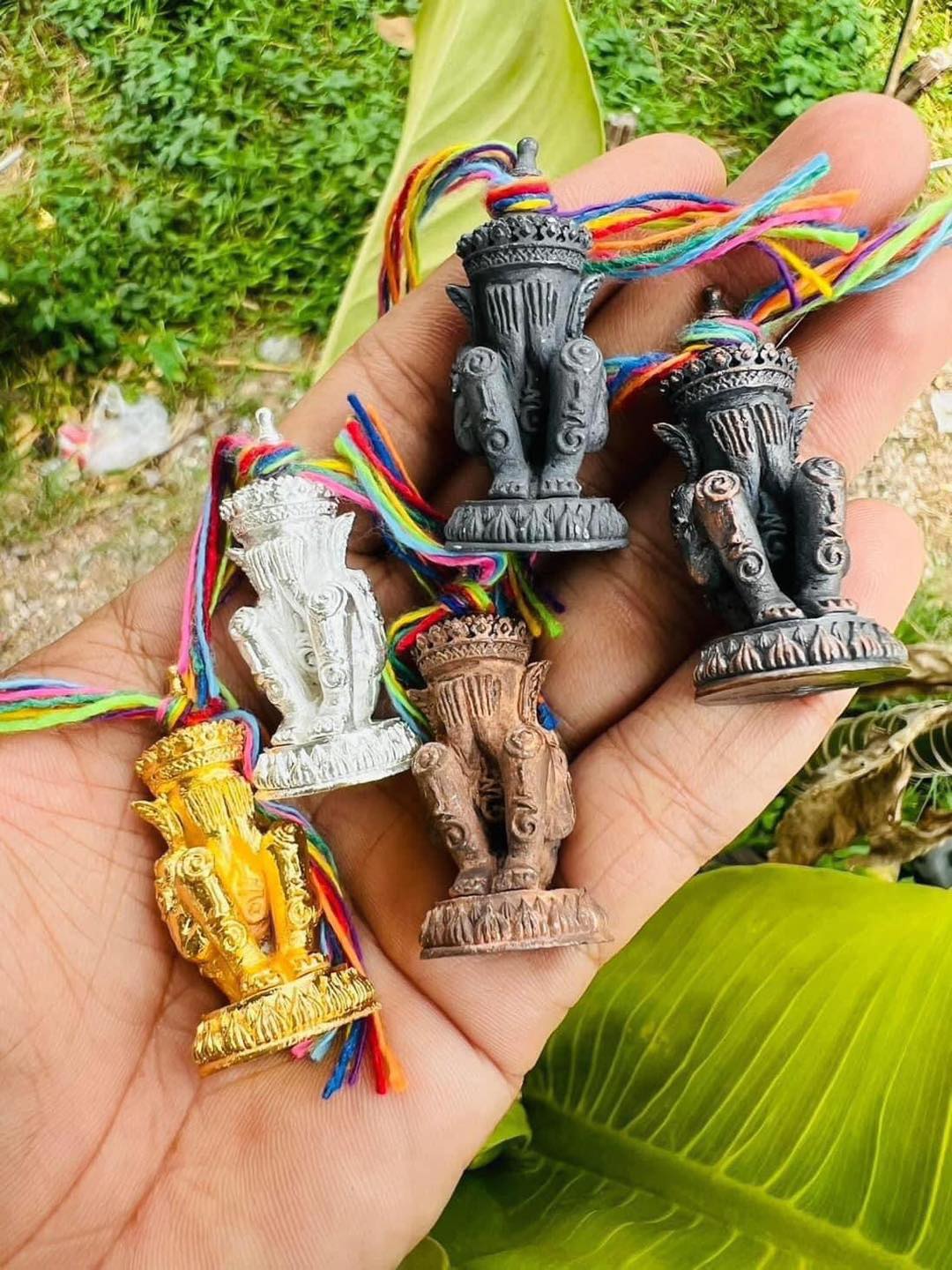 Hand holding five small Norah Chatri Pi Takta amulet for protection. Thai Blessing Co decorative amulets with colorful cords