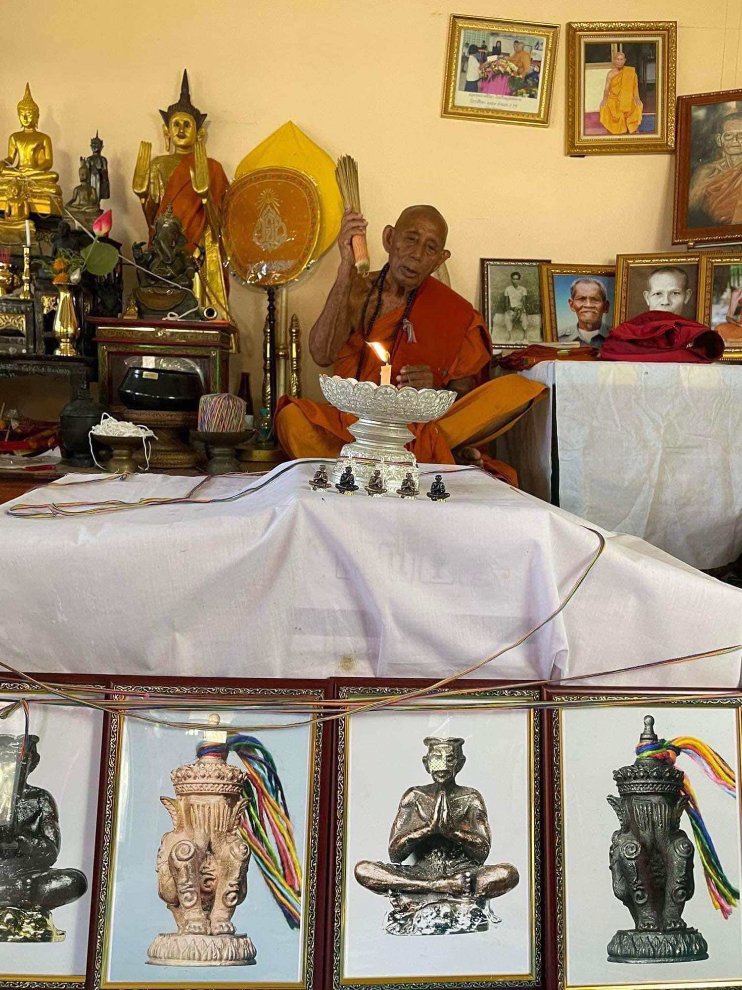 Monk blessing Norah Chatri Pi Takta amulet for protection. Thai shrine display with framed amulet statues and ceremonial offerings