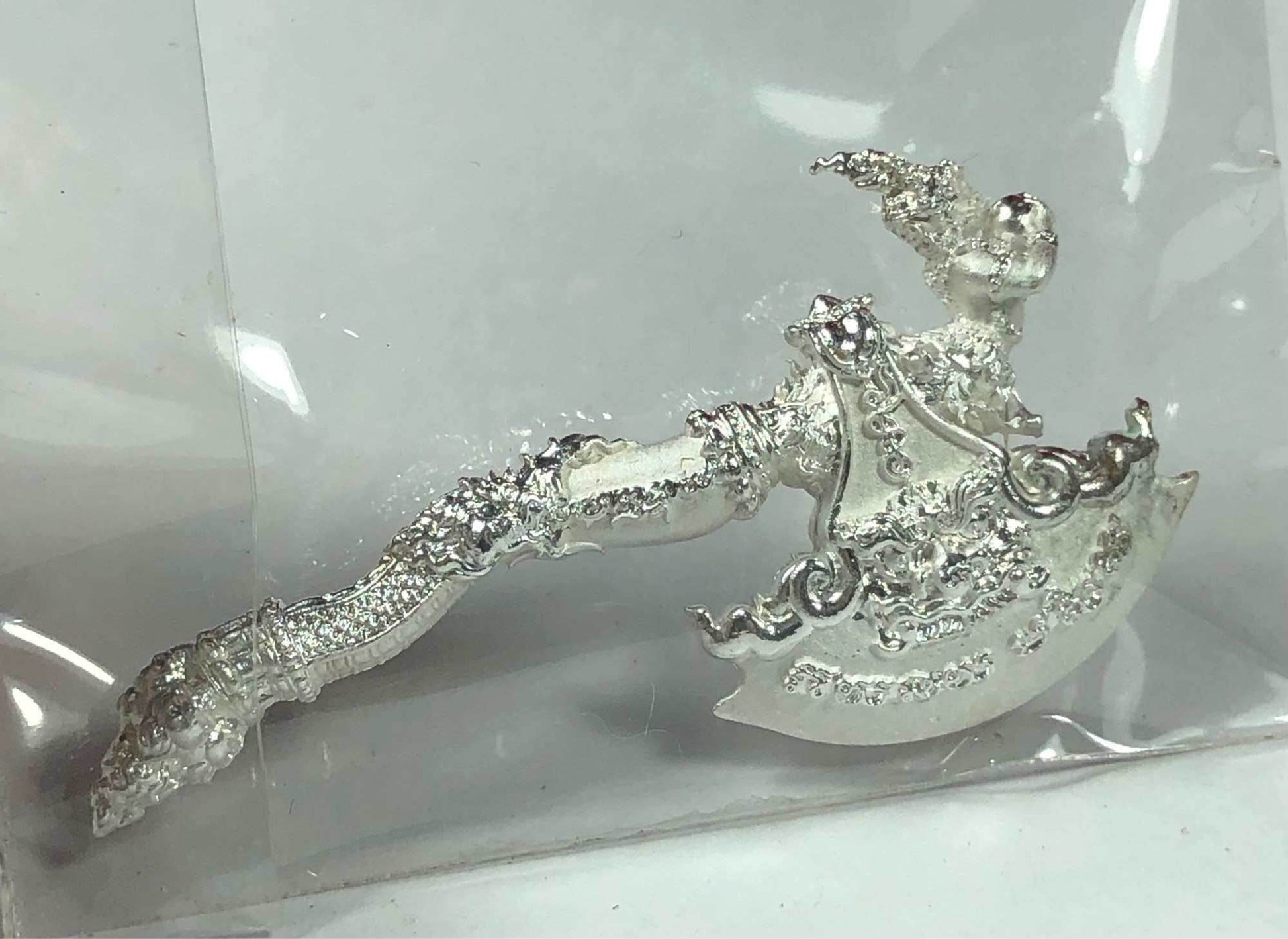 Silver ornate ceremonial axe amulet with Thai floral engravings on white background Phaya Khwan Maha Prap Amulet Tak Sila Edition