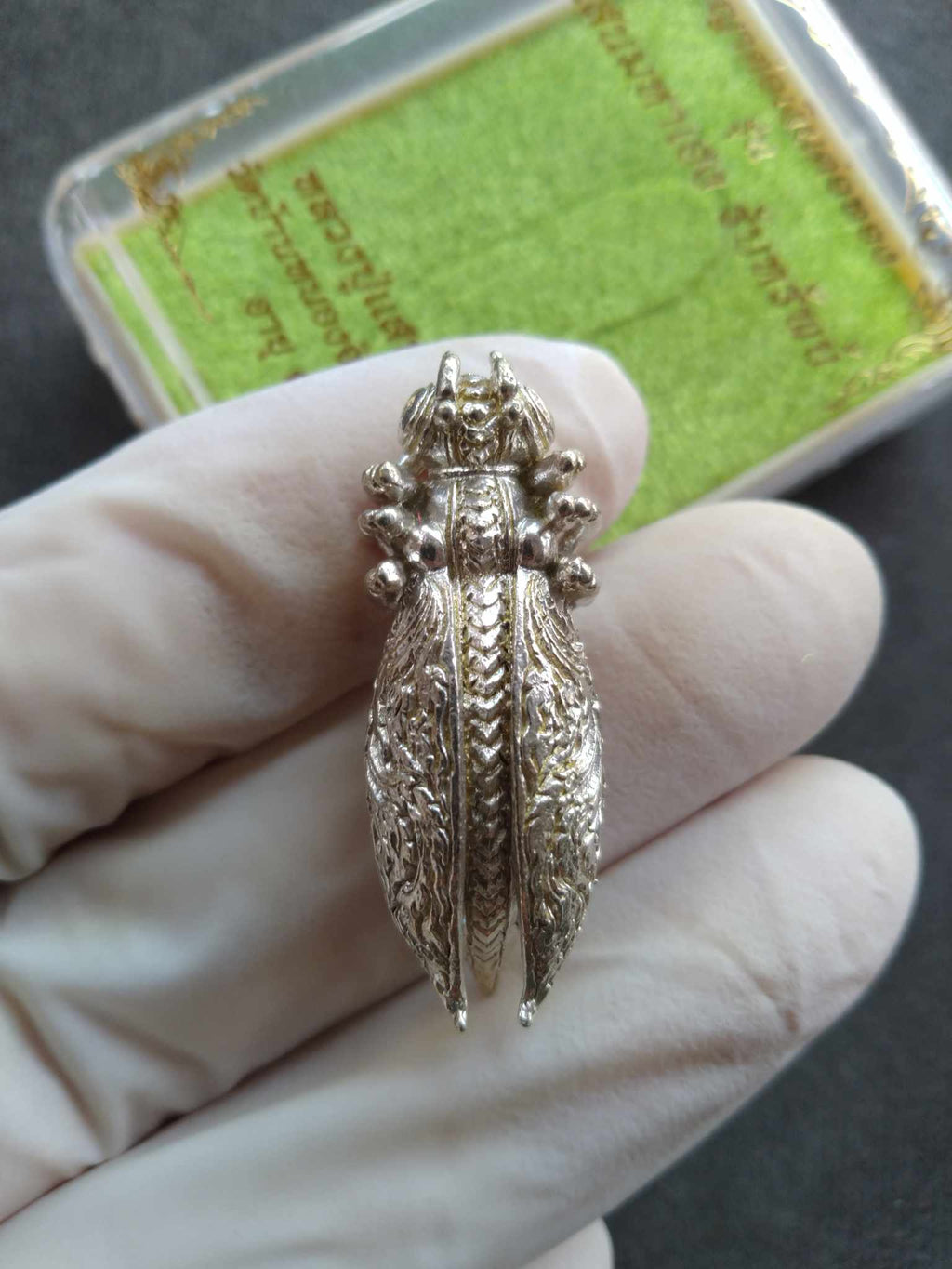 Silver Phaya Tor Ngern Tor Thong amulet pendant shaped like ornate cicada held in gloved hand