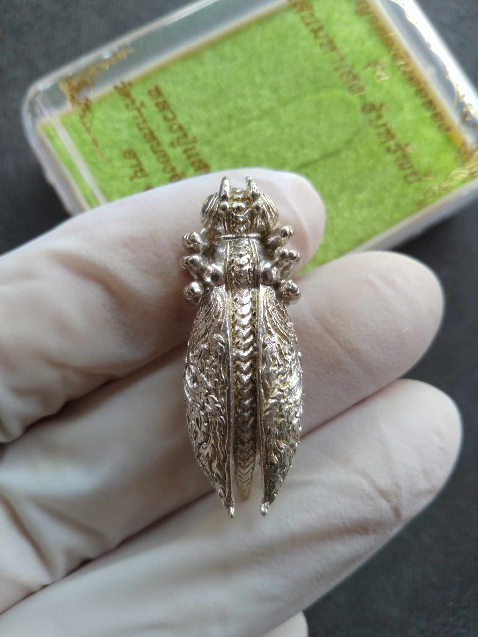 Silver Phaya Tor Ngern Tor Thong amulet pendant shaped like ornate cicada held in gloved hand
