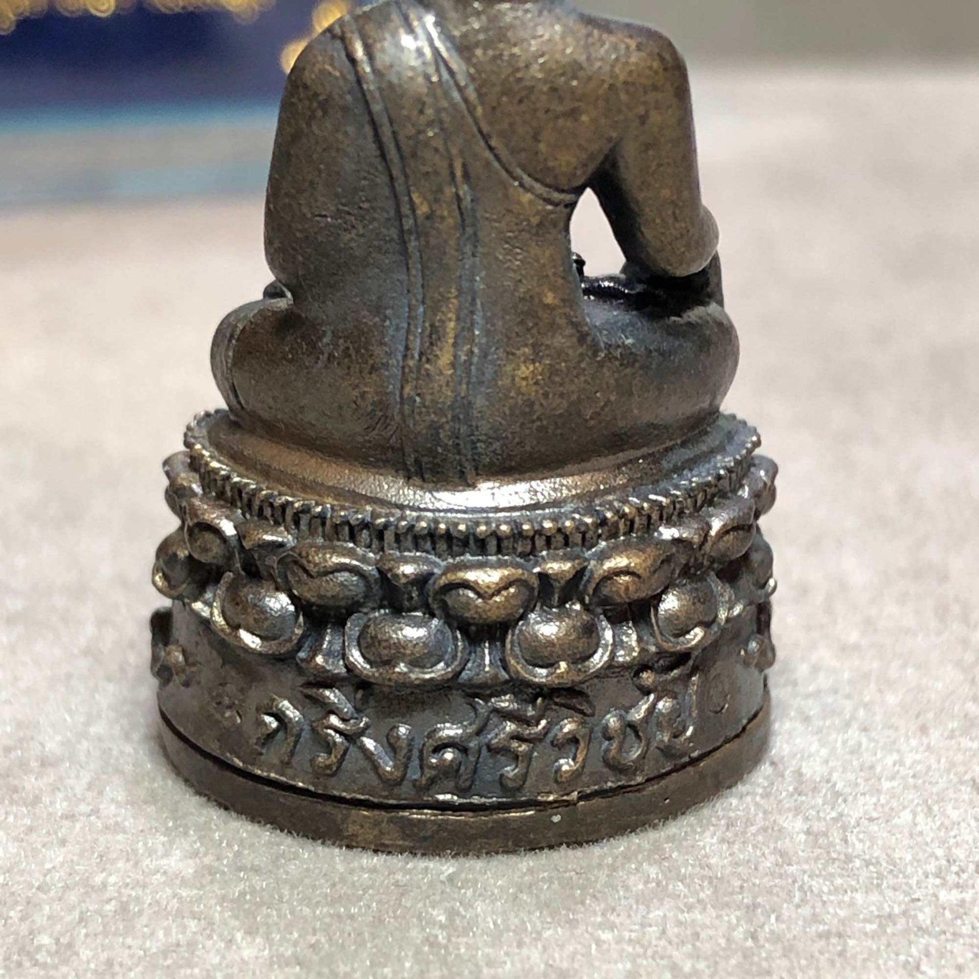 Back view of metal seated Buddha on ornate lotus base with Thai script showing Phra Kring Srivichai amulet