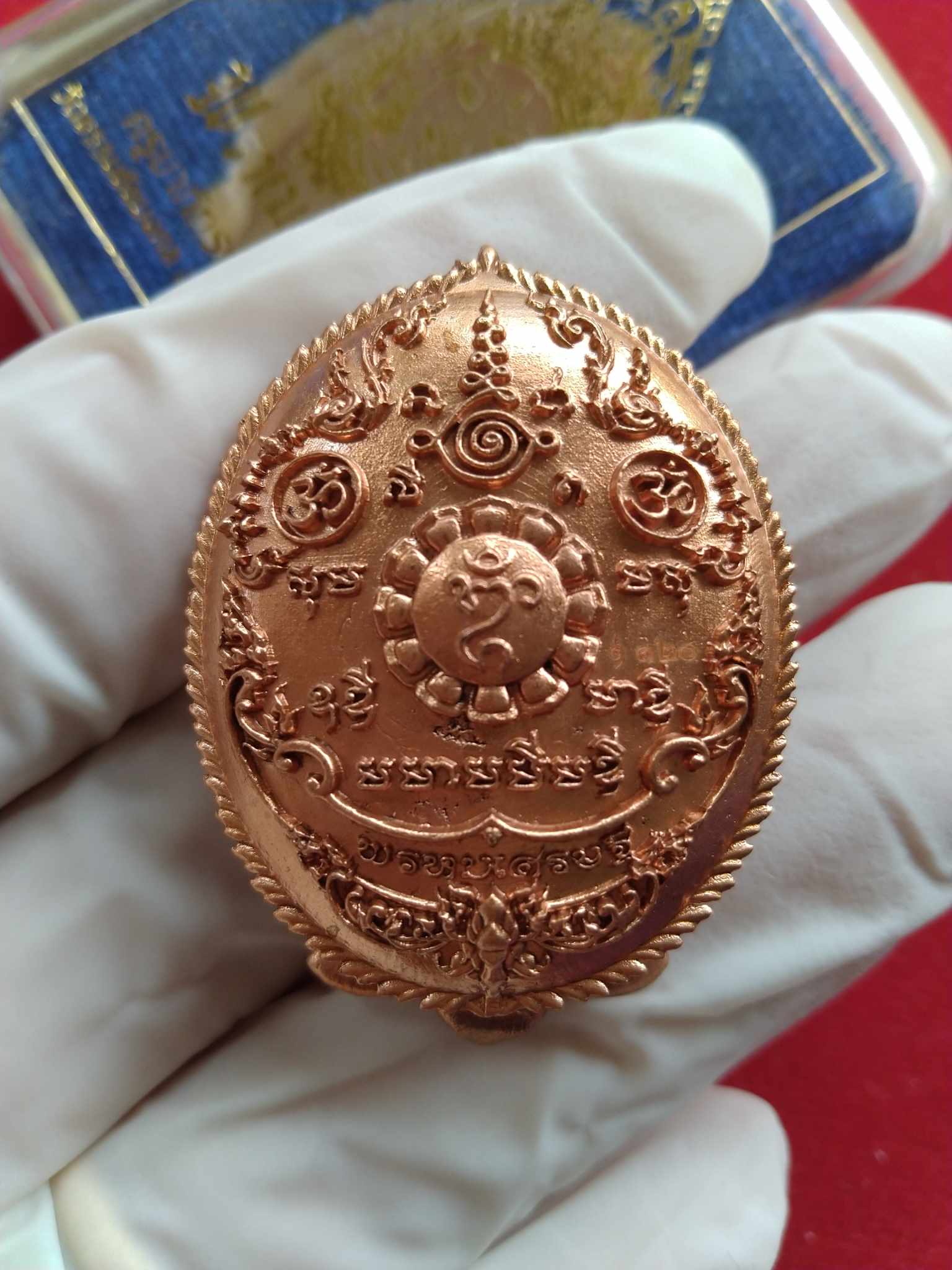 Phra Phrom amulet for wealth copper medallion pendant with intricate Thai engravings held in gloved hand