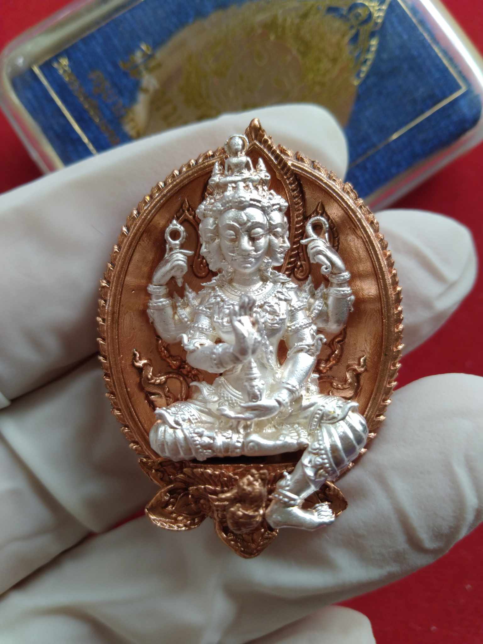 Thai Blessing Co Phra Phrom amulet for wealth silver deity pendant on copper frame held in gloved hand