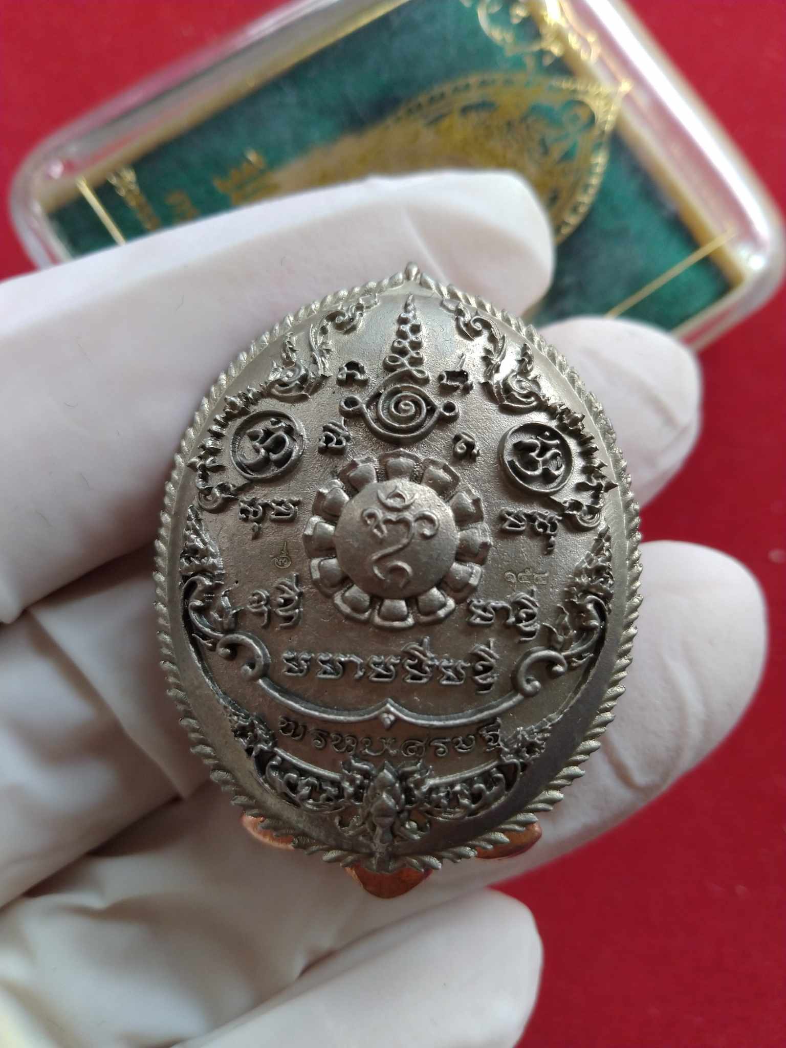 Phra Phrom Sethi amulet for wealth ornate silver oval Thai engraved pendant held in gloved hand