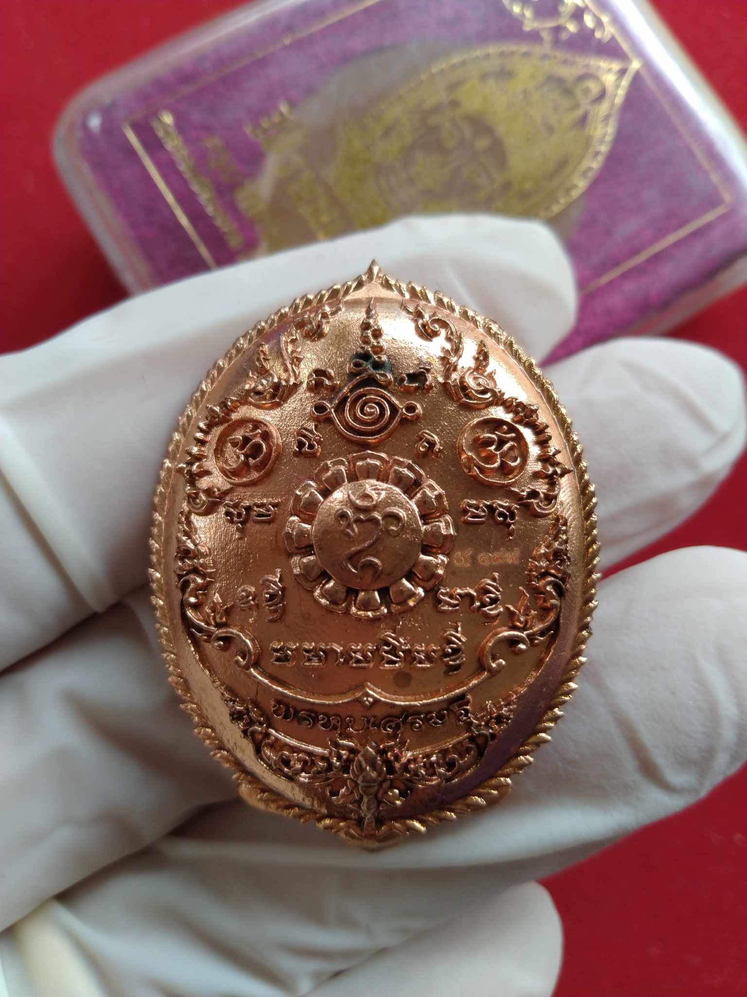 Phra Phrom Thai amulet for wealth copper oval medallion with intricate engravings held in gloved hand