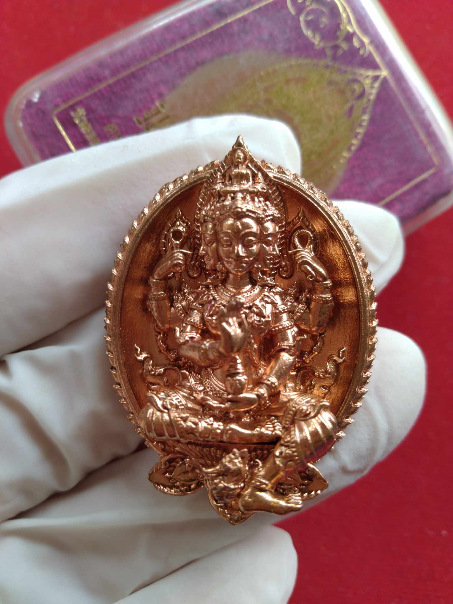 Phra Phrom Thai amulet for wealth copper colored ornate pendant held in gloved hand from Thai Blessing Co