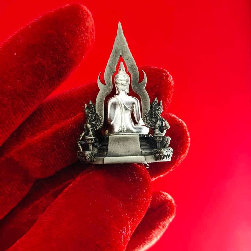 Silver Phra Phuttha Chinnarat amulet held on red velvet glove detailed Thai Buddha shrine design