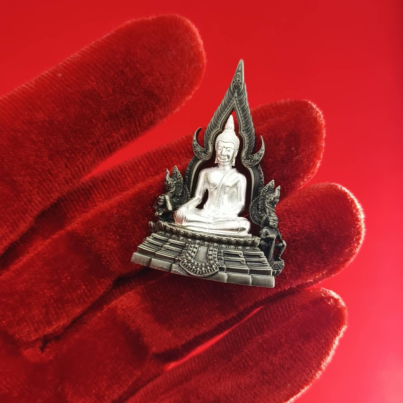 Silver Phra Phuttha Chinnarat amulet held on red velvet glove showcasing Thai devotional home decor