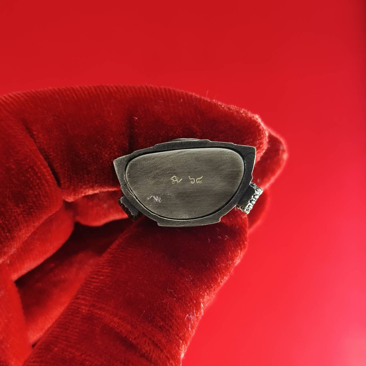 Phra Phuttha Chinnarat amulet metal back with engraved marks held in red velvet glove on red background