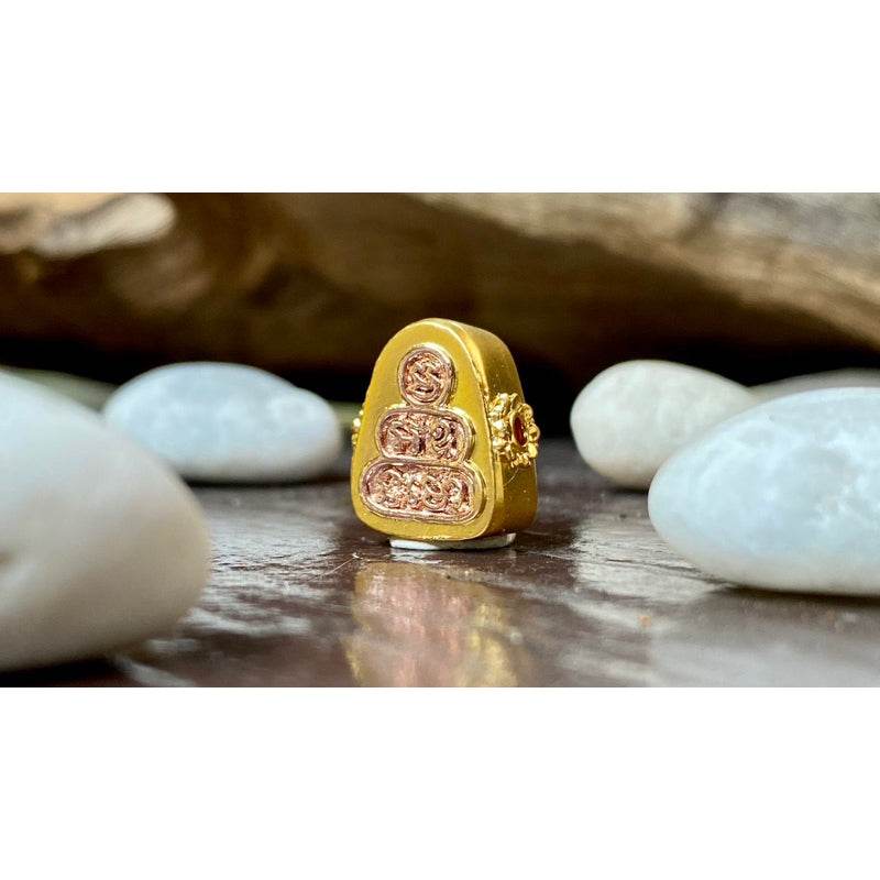 Phra Pidta amulet for sale gold Thai amulet with intricate relief on wooden table surrounded by white stones