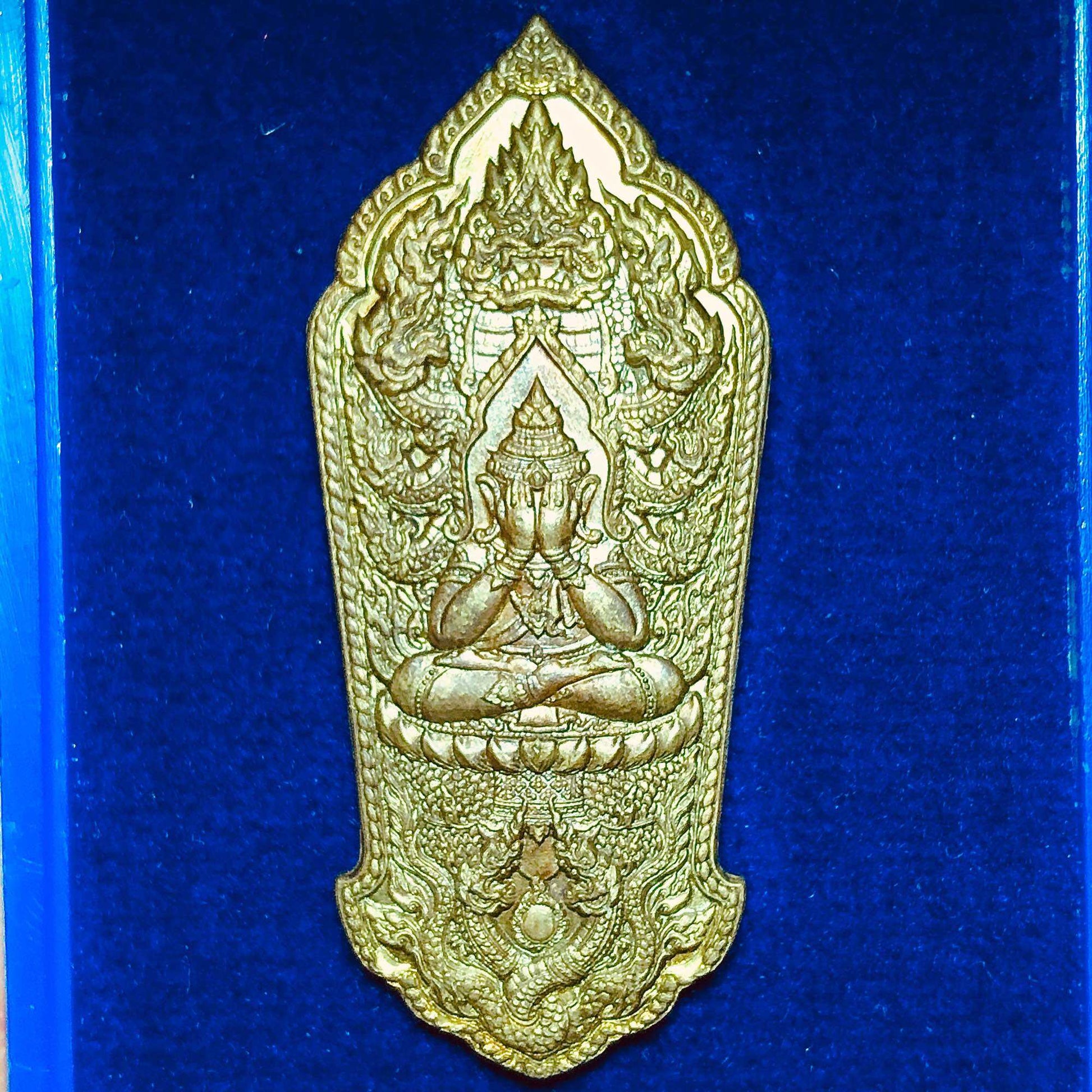 Gold shield Phra Pidta amulet with garuda and naga motifs on blue velvet Phra Pidta Maha Lap amulet for wealth