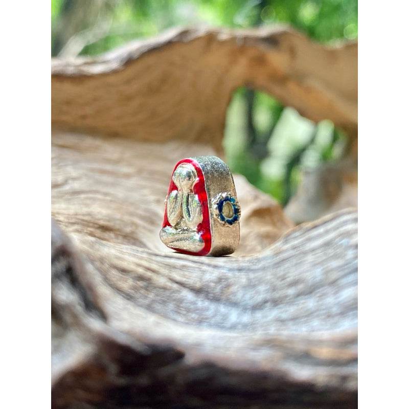 Thai Blessing Co Phra Pidta wealth amulet with red enamel edge and blue gem set on driftwood background
