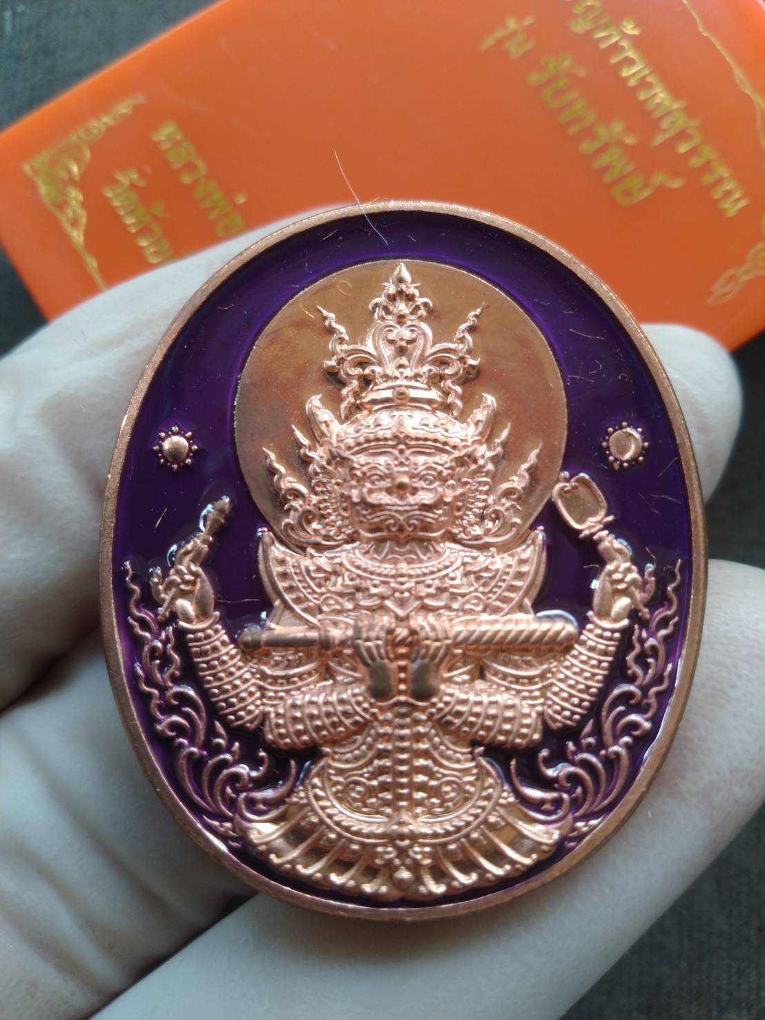 Phra Taw Wessuwan amulet for wealth copper oval pendant with purple enamel held in hand Thai Blessing Co
