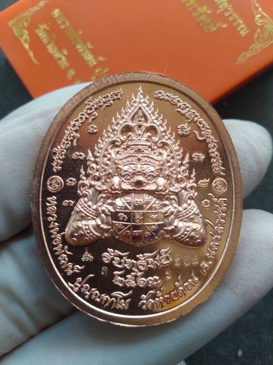 Handheld copper Phra Taw Wessuwan amulet for wealth coin medallion with guardian deity and Thai script
