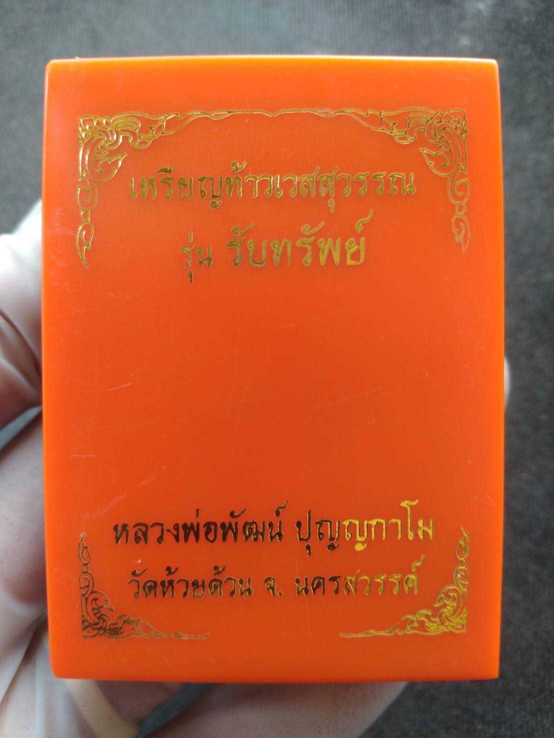 Phra Taw Wessuwan amulet for wealth orange presentation box with gold Thai script held in hand from Thai Blessing Co