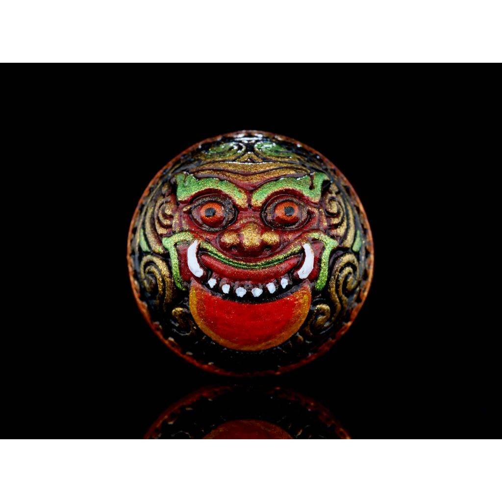 Colorful round Rahu Amulet bead with ornate demon face red tongue and gold green detailing on black background