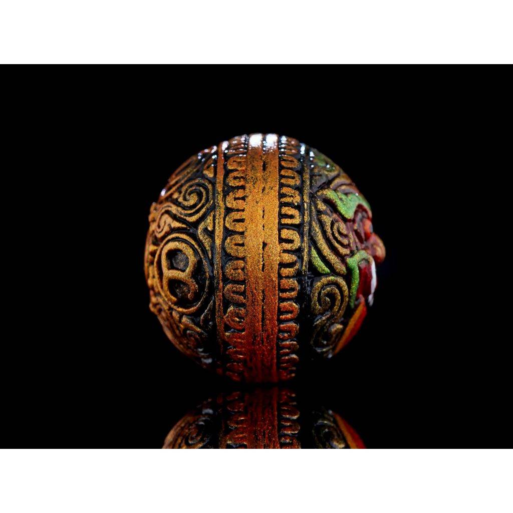 Ornate carved brass and colored bead Rahu Amulet with intricate Thai patterns on black reflective background