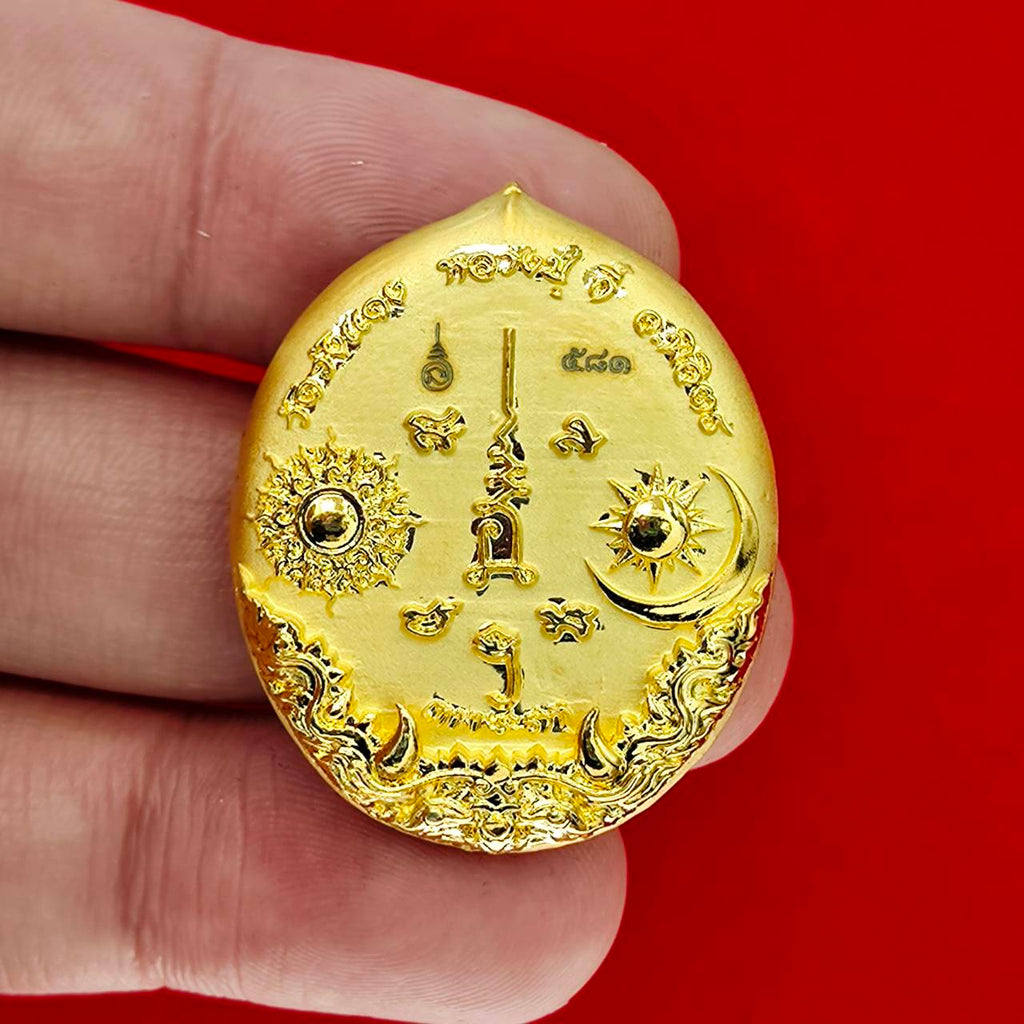 Gold oval Rahu deity amulet with sun and moon engravings ornate Thai script held between fingers