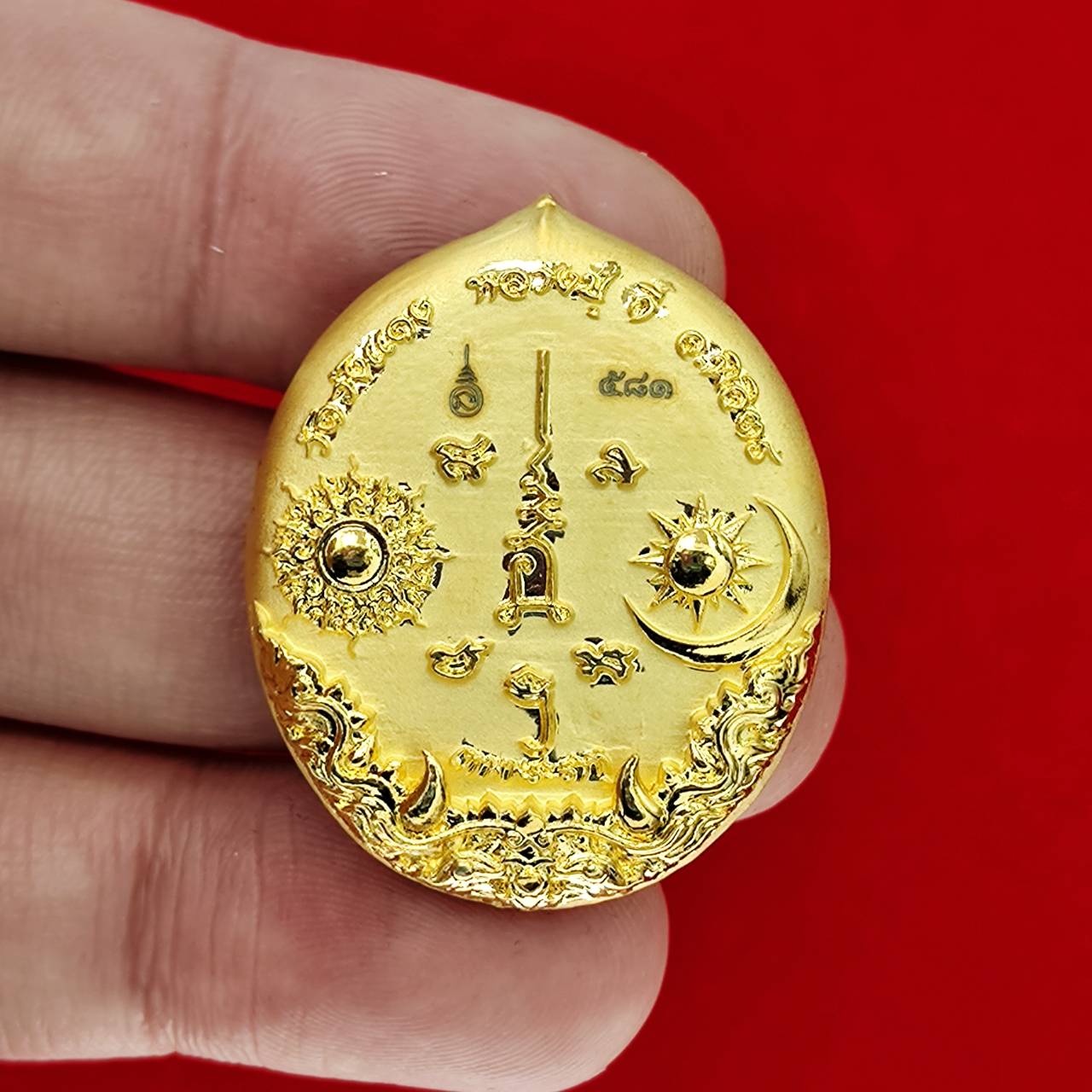 Gold oval Rahu deity amulet with sun and moon engravings ornate Thai script held between fingers