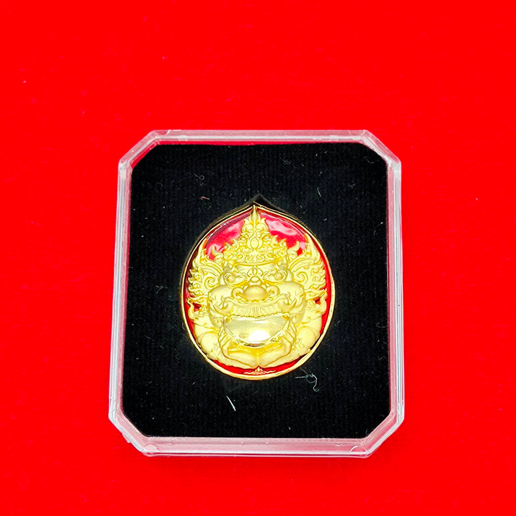 Ornate gold Rahu deity amulet medallion in clear display case on black velvet with red background