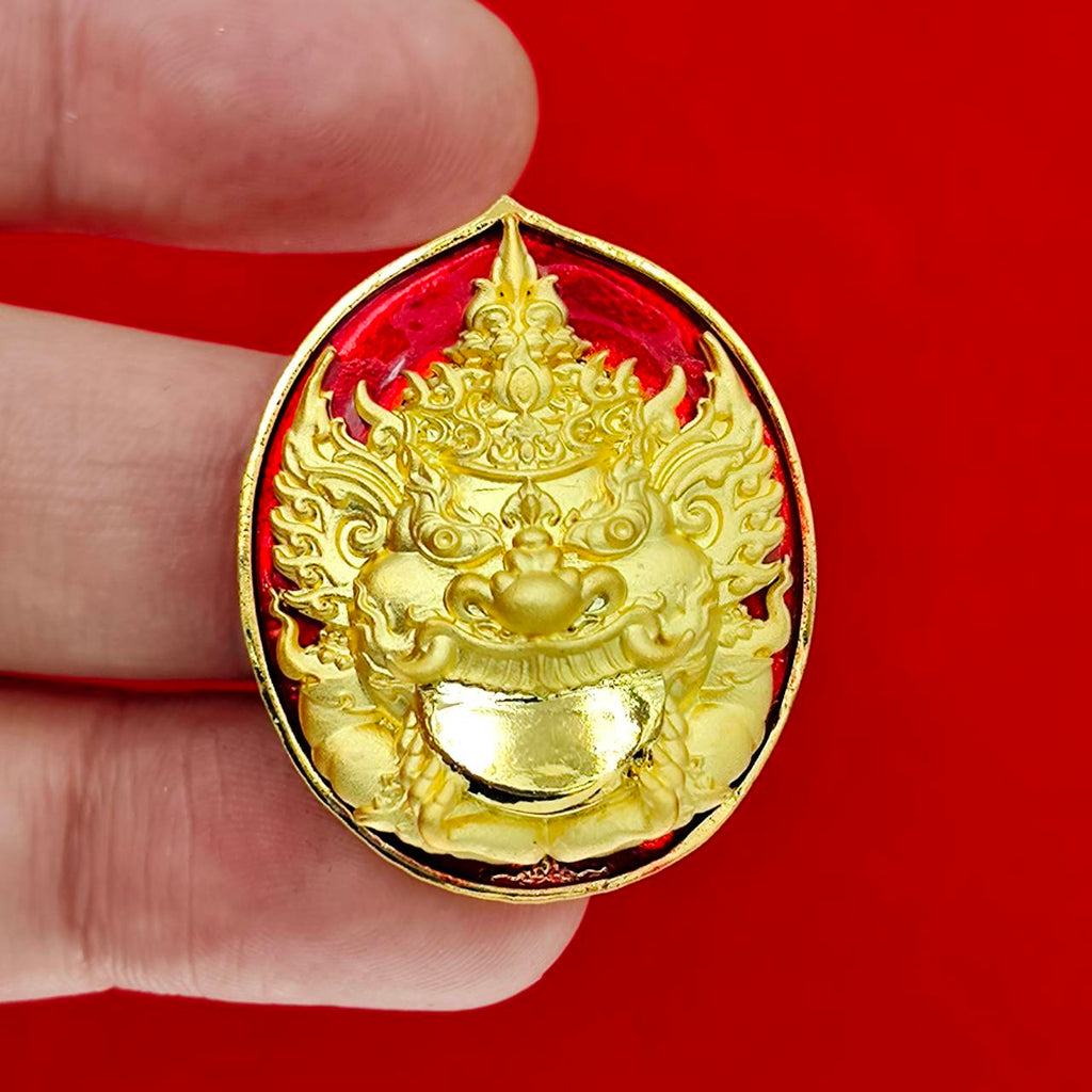 Handheld gold Rahu deity amulet on red enamel background Thai collectible decorative talisman