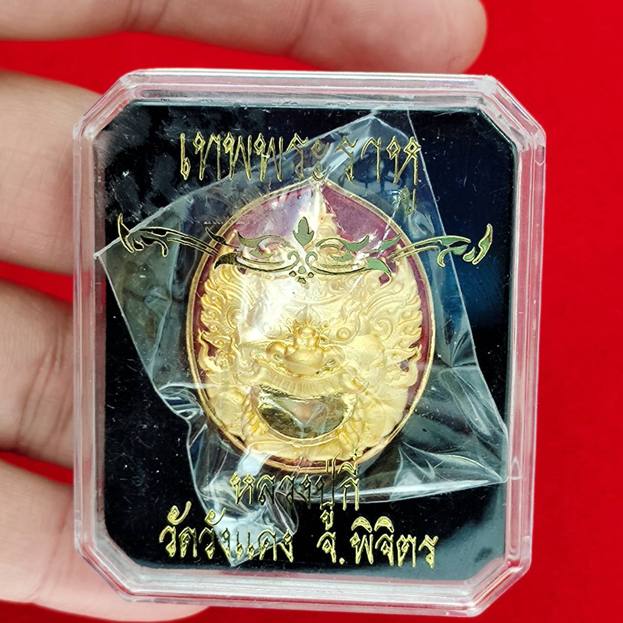 Rahu deity amulet gold medallion with ornate face in clear plastic display case held by hand