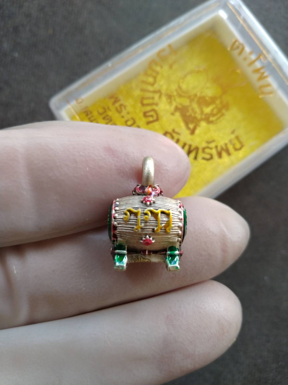 Sacred Drum Amulet for Wealth Prosperity Blessed by Phra Ajarn Tao. Gold drum pendant with red green enamel held in gloved hand