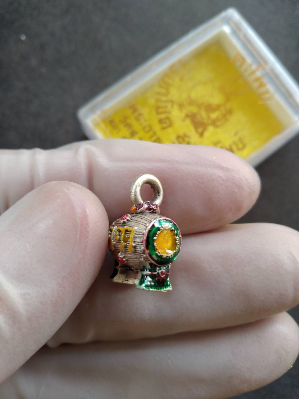 Small gold green Sacred Drum Amulet for Wealth Prosperity Blessed by Phra Ajarn Tao. Pendant held between fingers