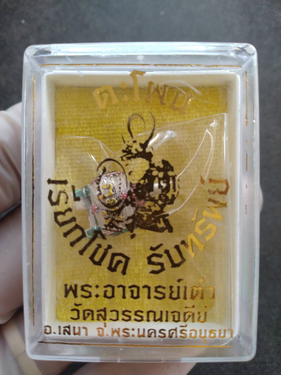 Clear display case with gold backed Sacred Drum Amulet for Wealth Prosperity Blessed by Phra Ajarn Tao. Thai Blessing Co product