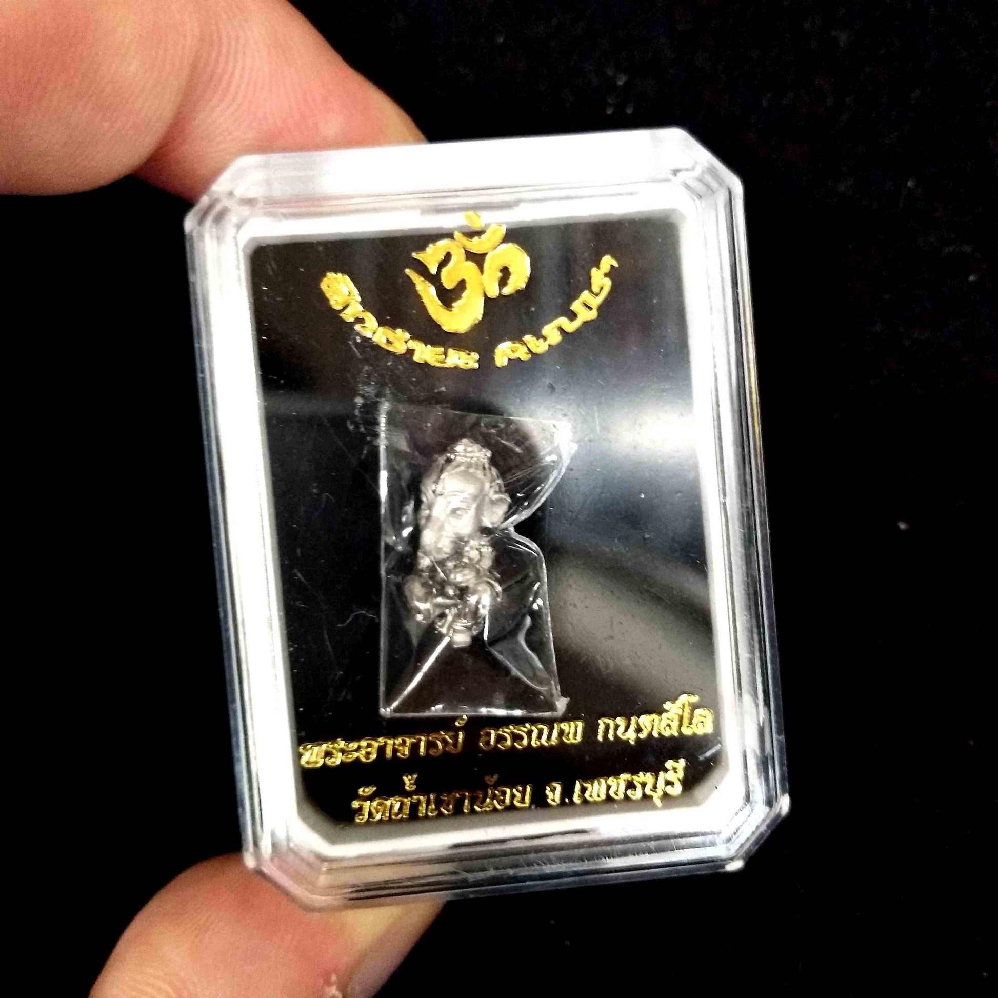 Sacred Thai Ganesh pendant silver amulet in clear display box with gold Thai script held between fingers